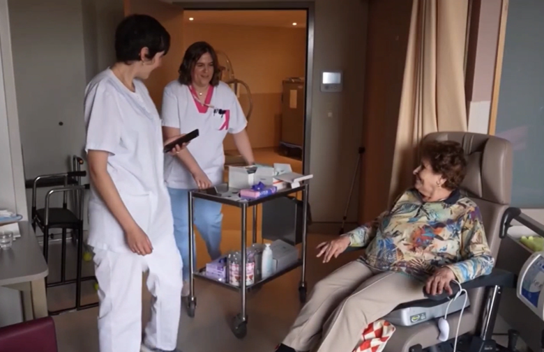 Chariot de soins bucco-dentaires en EHPAD Soignants en EHPAD entrant dans la chambre d’une résidente avec un chariot de soins bucco-dentaires pour réaliser un examen bucco-dentaire visuel.